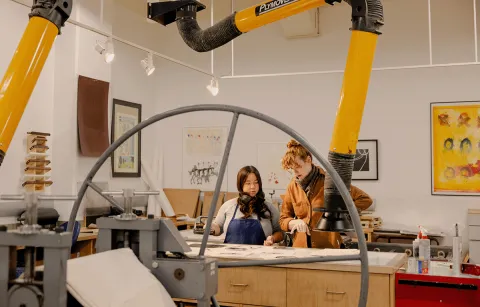 Instructor and student looking at prints on a table in a printmaking studio class
