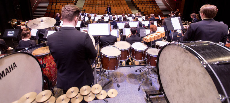 Wind orchestra performing on stage, view from percussion section