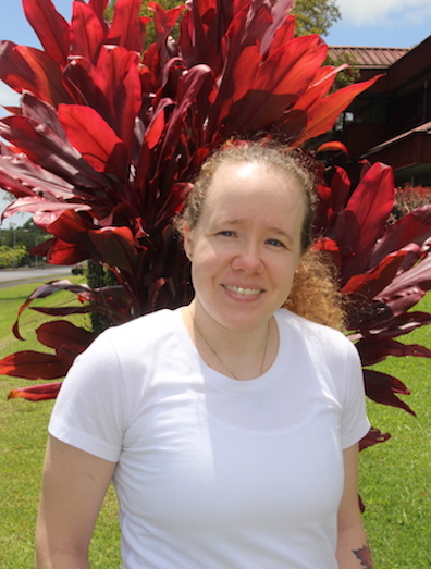 A woman in a white t-shirt standing in front of red shrubbery