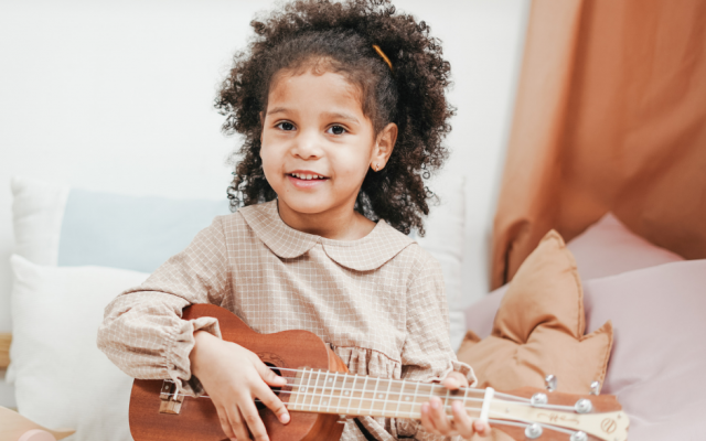 Little girl playing a ukulele and smiling at the camera