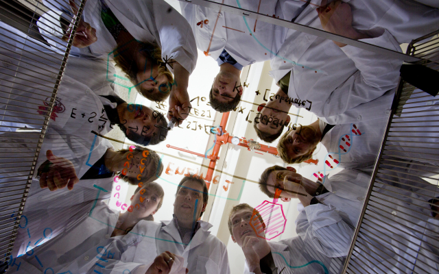Group of students hovering over glass table writing equations