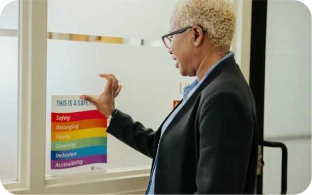 Woman smiling and pinning a rainbow sign that says "This is a Safe Place"