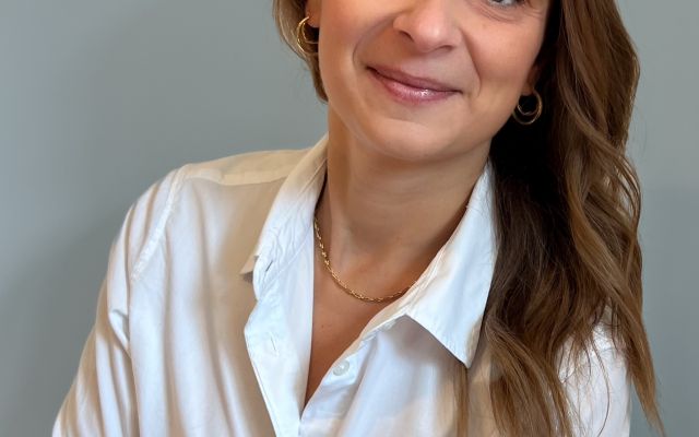 Picture of Elizabeth Cavaliere from the waist up; she has long brown hair and is wearing a white shirt.