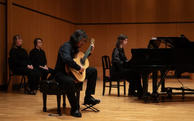 Students, dressed in black, playing the guitar and piano on a stage
