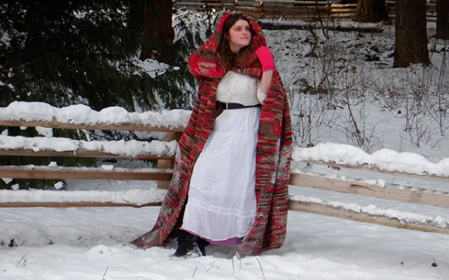 photo of Olympia Tomasta wearing a white dress and red hooded cape standing in a snowy background.