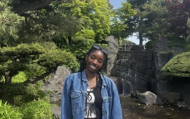 A photo of Mmeso standing in front of lush greenery and a small manmade pond with a waterfall feature.