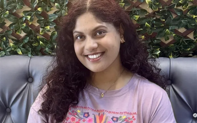 Photo of Afifa wearing a purple floral shirt in front of a leafy background