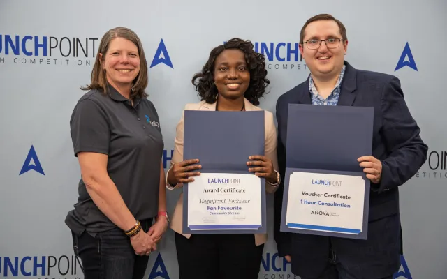 Three people holding two certificates in front of a blue background