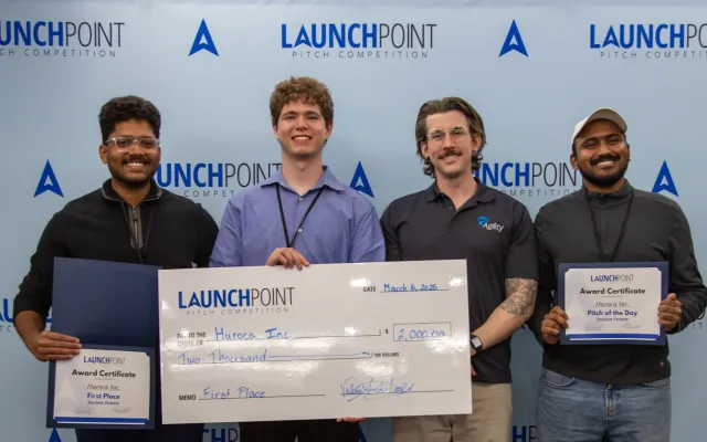 four men holding a large cheque and two certificates in front of a blue backdrop