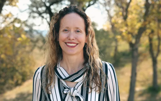 A woman in a blouse, standing in front of trees
