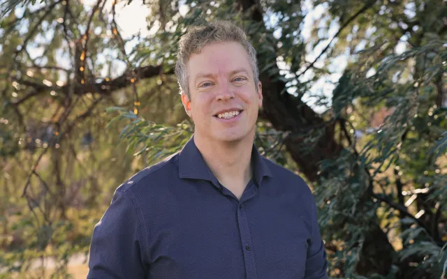 A man stands in front of a Russian olive tree