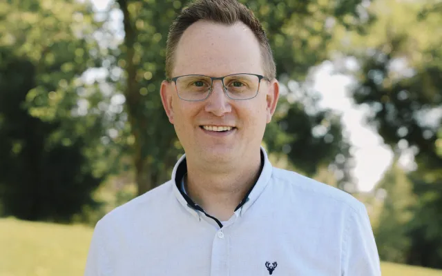 A man stands in front of a cluster of trees