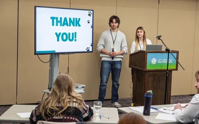 Two students behind a lethbridge polytechnic podium in front of a screen displaying the text THANK YOU!