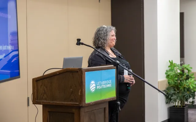 Student standing behind a Lethbridge Polytechnic podium with a microphone in hand, smiling towards the audience