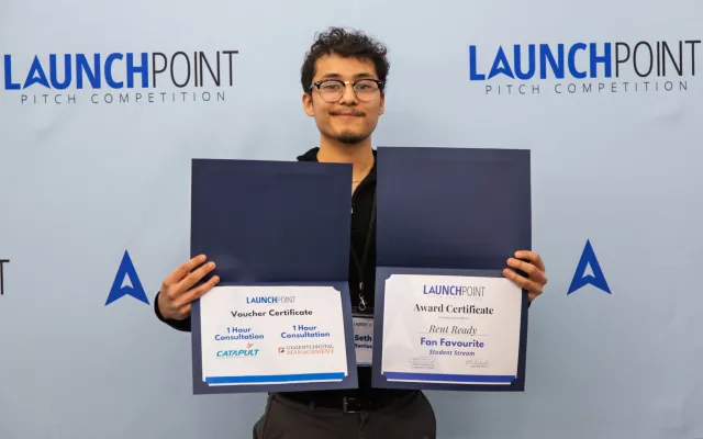 Young man holding two certificates in front of a blue backdrop