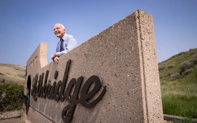 Dennis Connolly leaning over the welcome to Lethbridge concrete sign, looking off into the distance and smiling