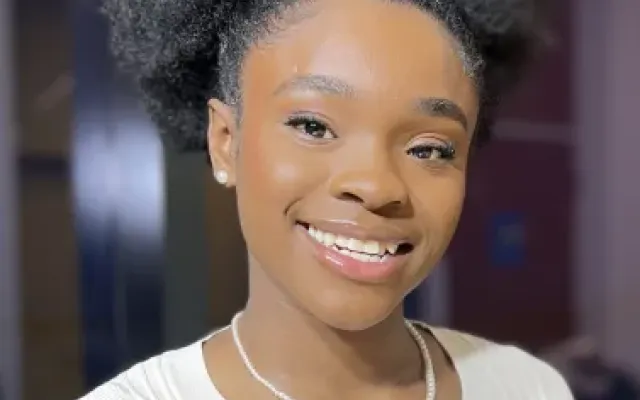 Kimoya wearing a white shirt and a pearl necklace.
