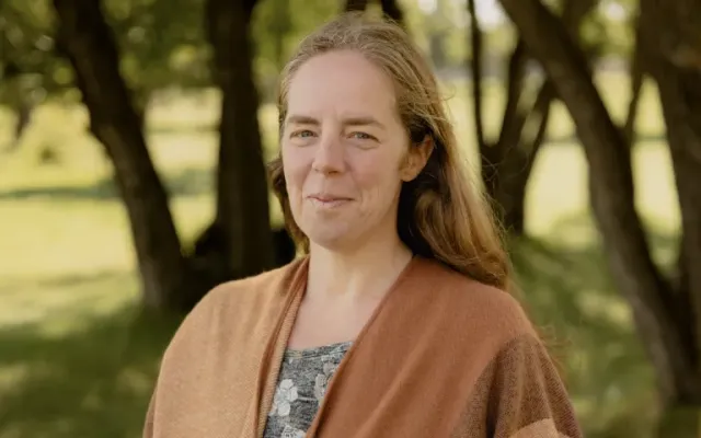 Rebecca wearing a brown shawl standing in front of trees.