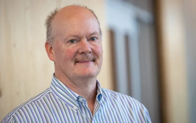 man in a stripped button up in front of a door