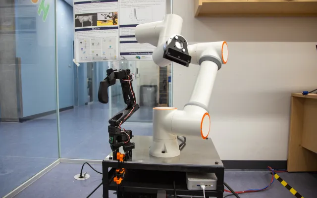 A large robot arm attached to a table, next to a smaller prototype of the same arm