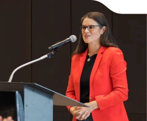 Tara MacDonald standing at a podium speaking