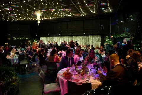 Abbondanza 2026. A set of tables with string lights and a group of people sitting down.