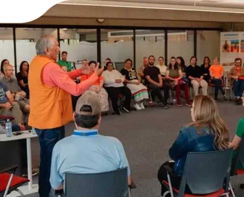 Dr. Leroy Little Bear speaking to a room of people seated in a circle