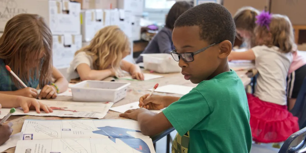 Boy in green shirt writing in a school workbook