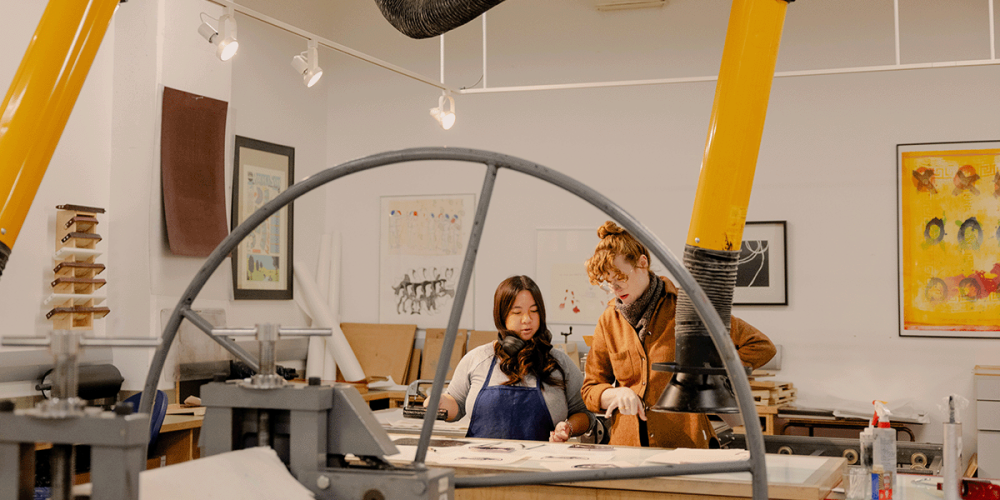 Instructor and student looking at prints on a table in a printmaking studio class