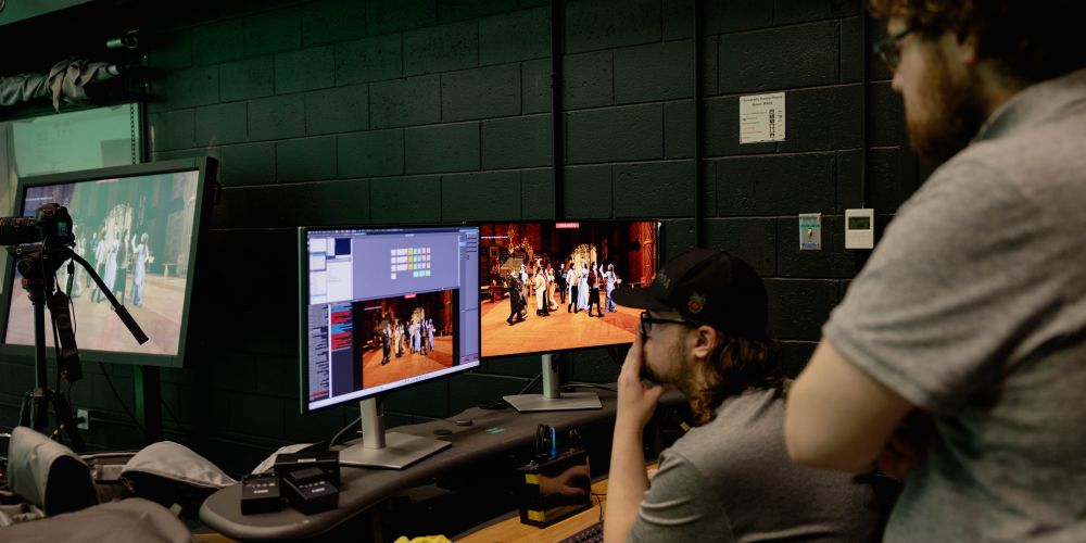 Students work on a computer in a green screen room.