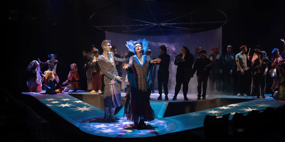 scene from ULethbridge Drama Mainstage show called "AI, Avatars & Aliens: A Speculative Cabaret". People in futuristic costumes on a tri-split catwalk with projected stars.