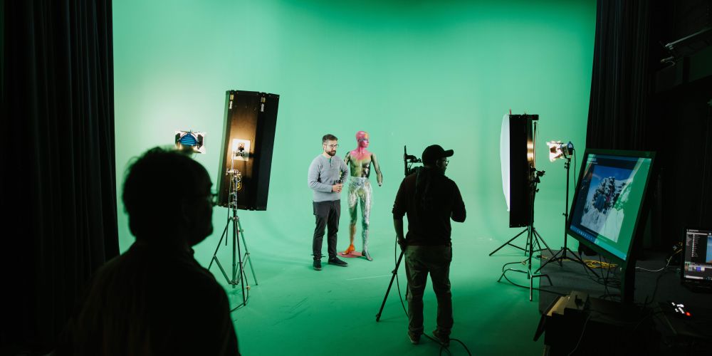 People setting up cameras and lights in a green screen room.