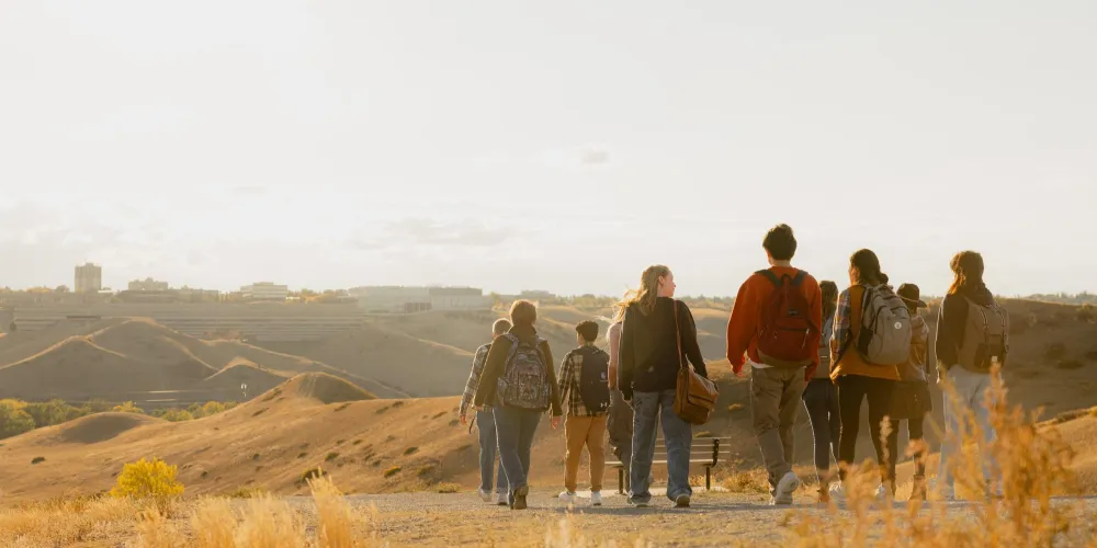 Students walking down a coulee trail with the University of Lethbridge in the background