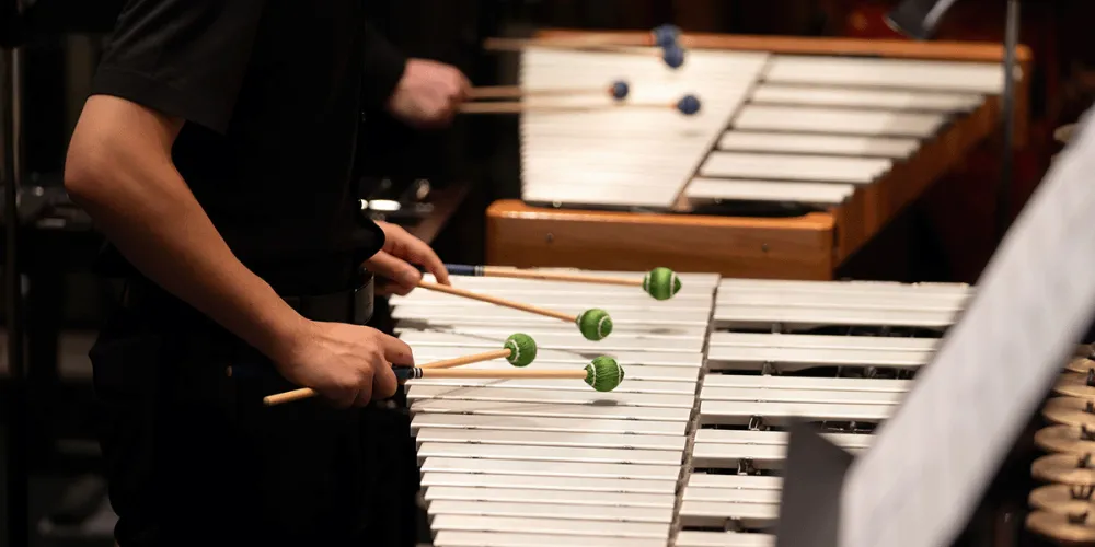 close up of two people playing on glockenspiels using green mallets