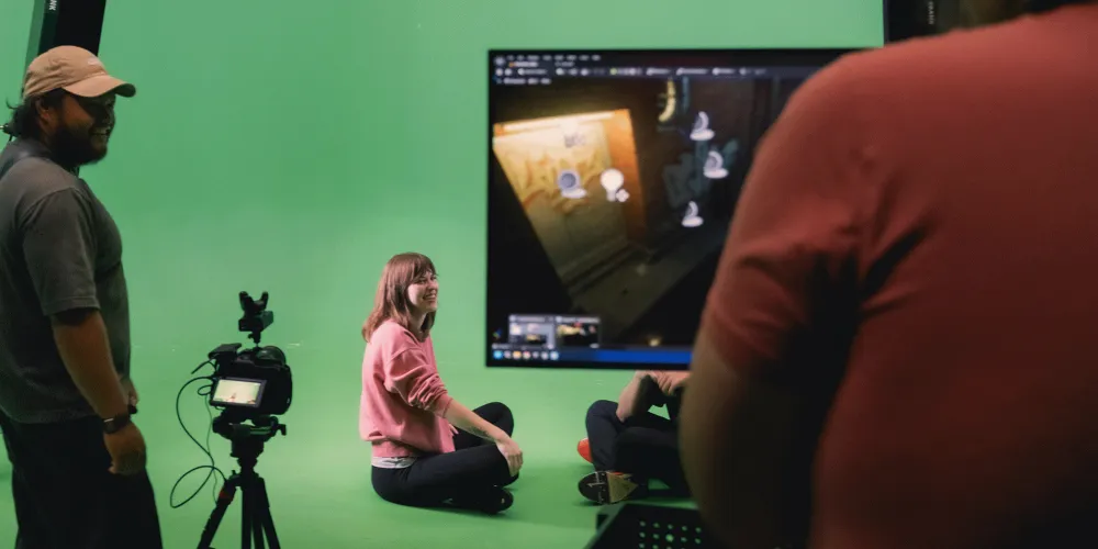 a person is sitting on the floor for video shoot in front of a green screen.