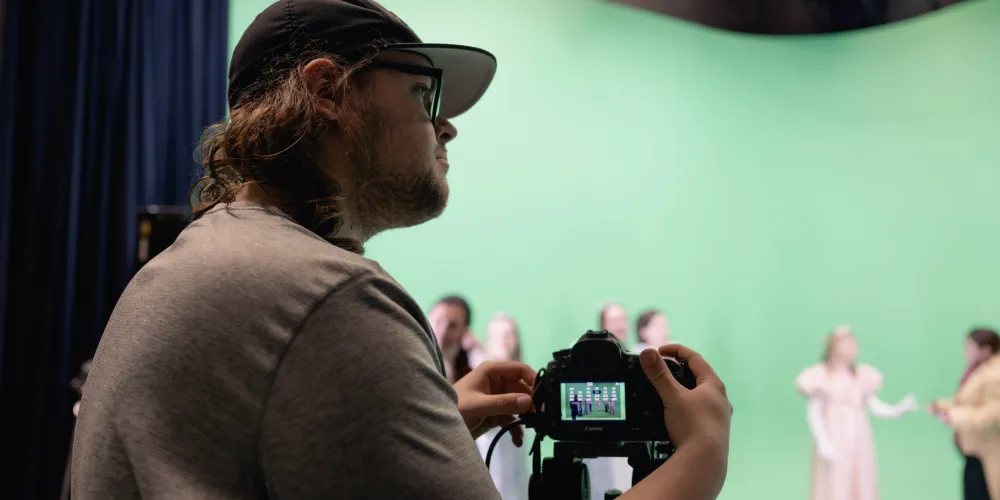 Cinema and Media Studies - student pointing a camera at actors in front of a green screen