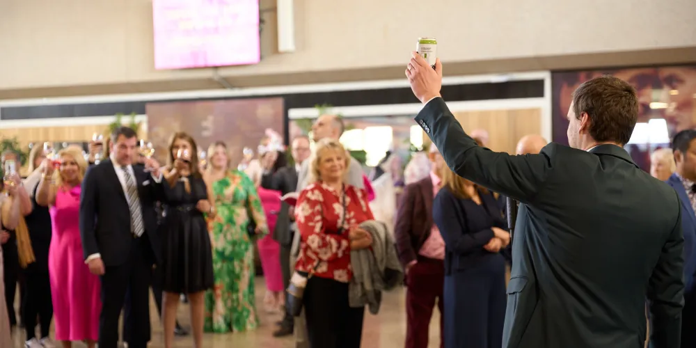 A man in a suit gives a toast to a crowd of people in the University Hall Atrium at Abbondanza.