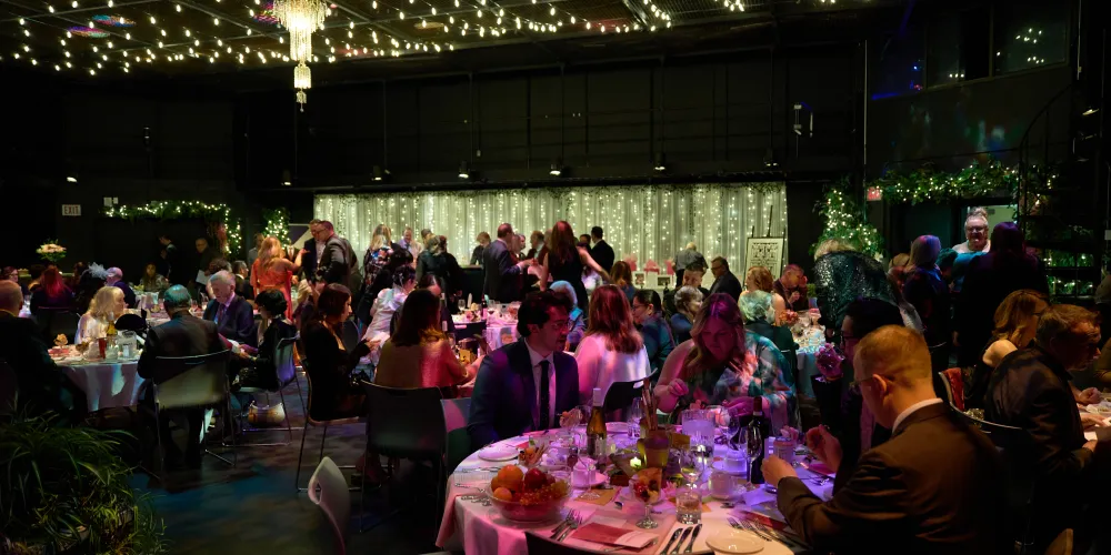 Abbondanza 2026. A set of tables with string lights and a group of people sitting down.