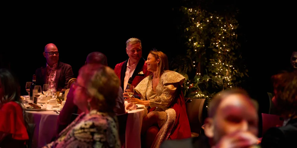 A man wearing a crown sitting next to a woman in a dress.