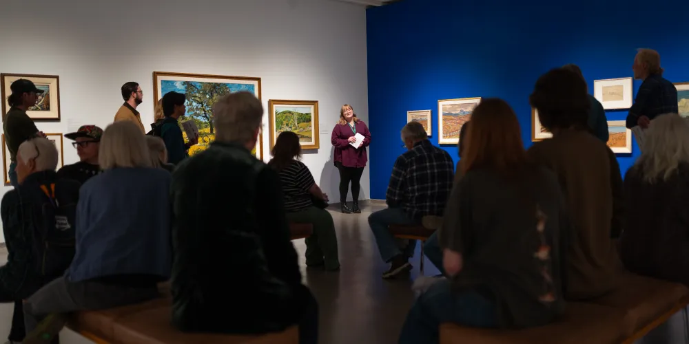 A group of people sitting in an art gallery listening to a woman give a talk.