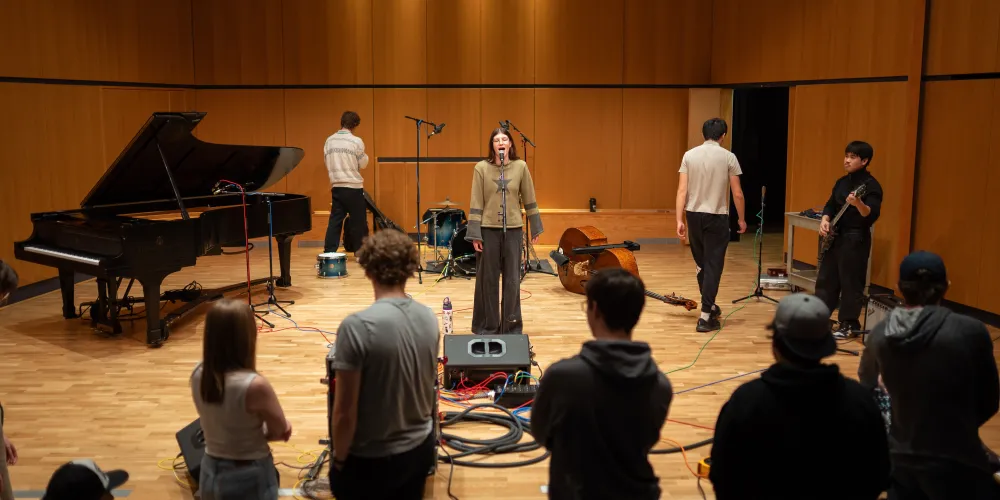 A group of students working with audio equipment in a recital hall.