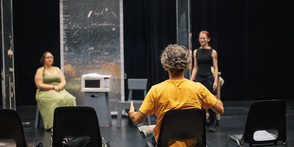 A man sits in a chair talking to student actors.