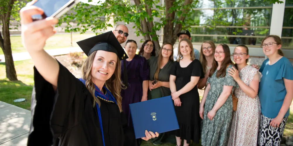 A photo of a grad taking a selfie with her family in the background.