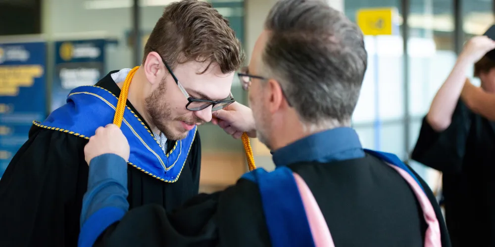 A faculty member drapes gold cords (signifying great distinction) over the neck of a grad.
