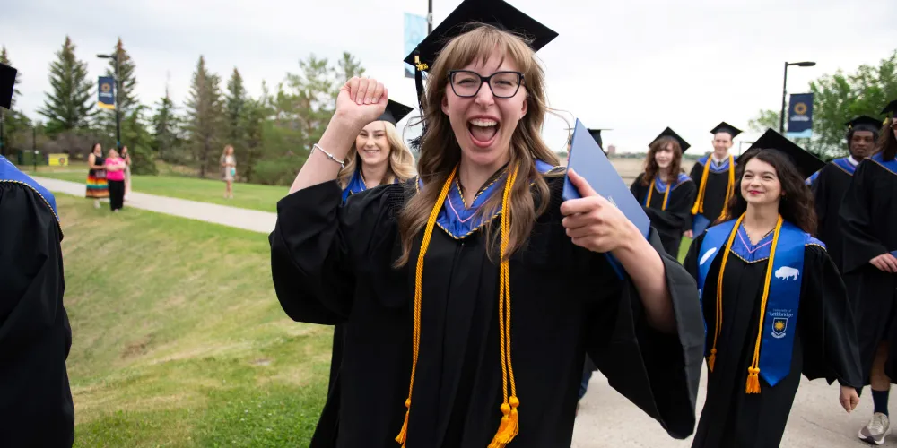 A grad cheering as they walk in the procession line outdoors