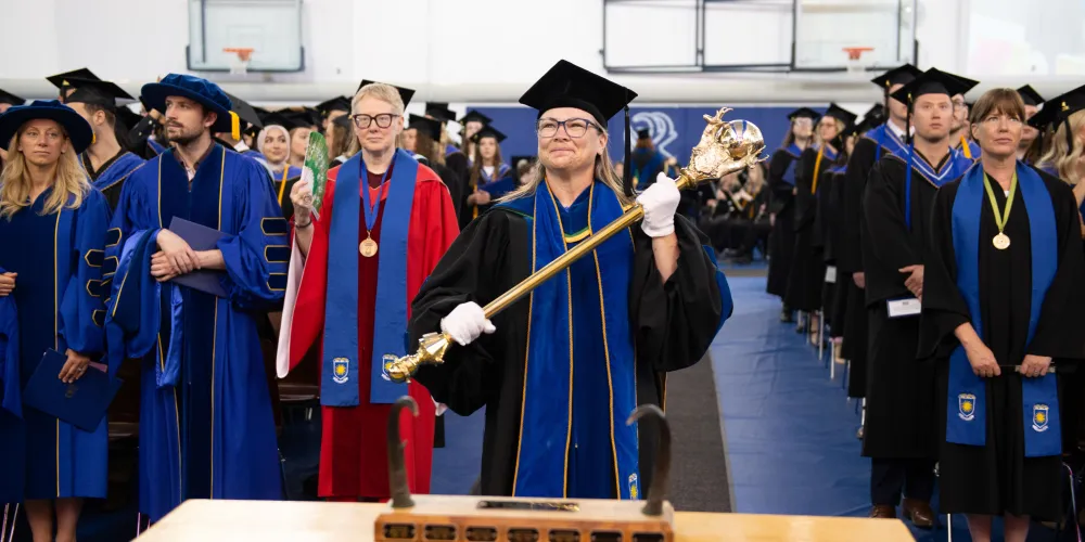 The Chief Marshal holds our mace as she leads the procession line into the gymnasium, marking the beginning of the ceremony.