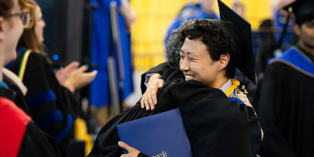 Grad hugging a faculty member during the ceremony