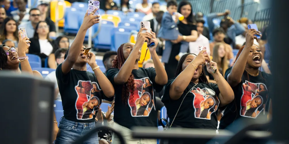 Four guests cheering and filming with their phones. Each wears a shirt with their grad's face on the front.