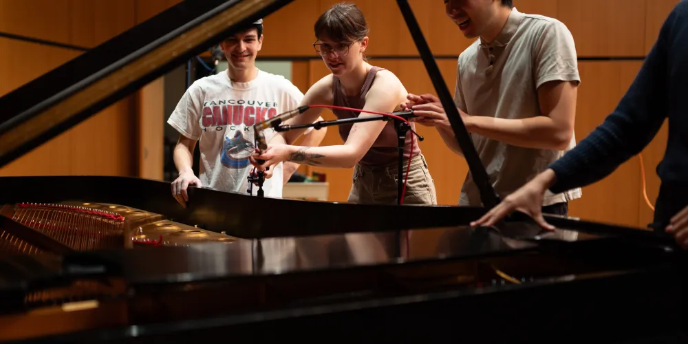A group of students setting up a microphone at a piano