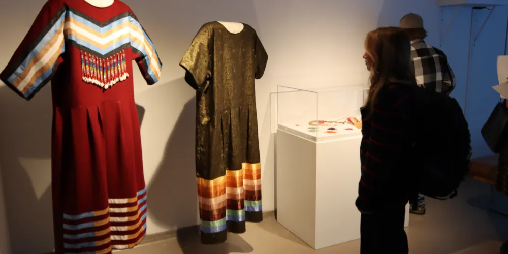 A student looks at Indigenous dresses in a gallery exhibition